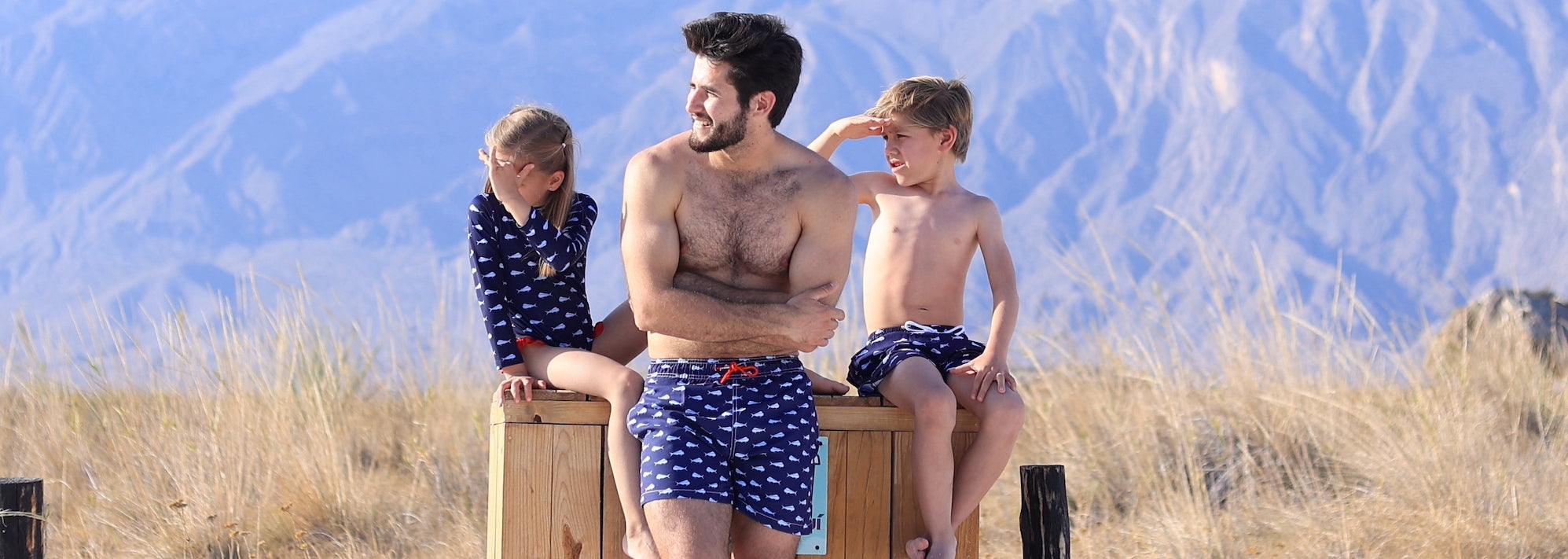 foto de modelos usando trajes de baño family match color azul marino con print de la marca tintarella coleccion mahi mahi disponible para niño,niña, hombre y mujer